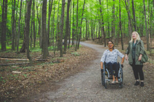 Deux femmes dans la forêt se promènent l'une est en fauteuil roulant manuel l'autre debout à côté d'elle