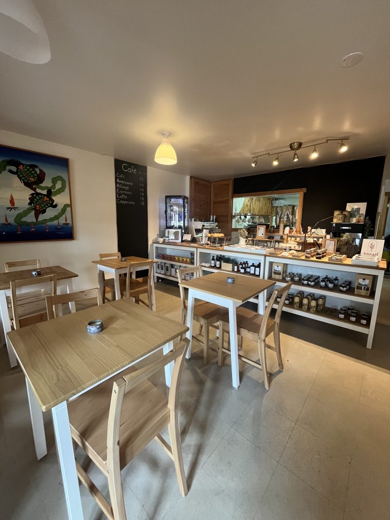 Intérieur d'une pâtisserie avec des tables en bois, des étagères remplies de confitures et de produits artisanaux.