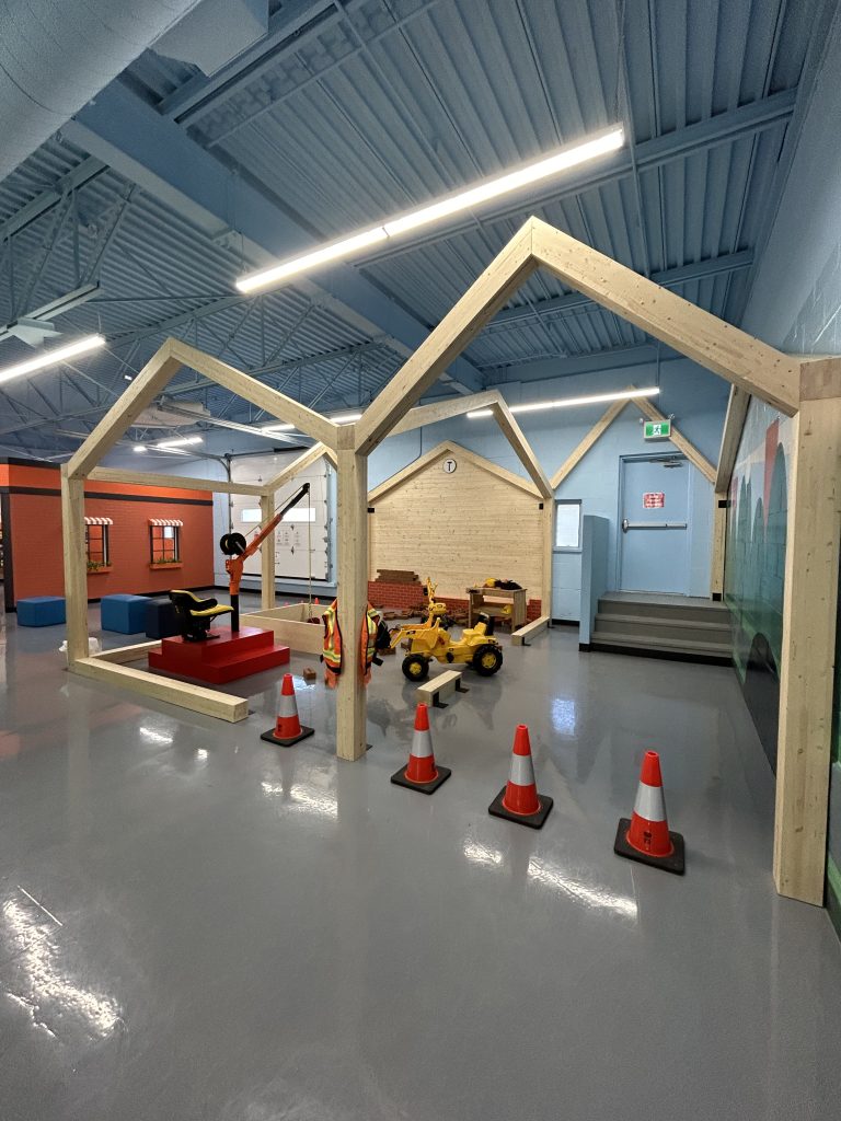 Espace de jeu intérieur pour enfants avec des structures en bois en forme de maisons, des jouets de construction et des cônes orange, au P’tit Monde des Grands dans les Cantons-de-l’Est.