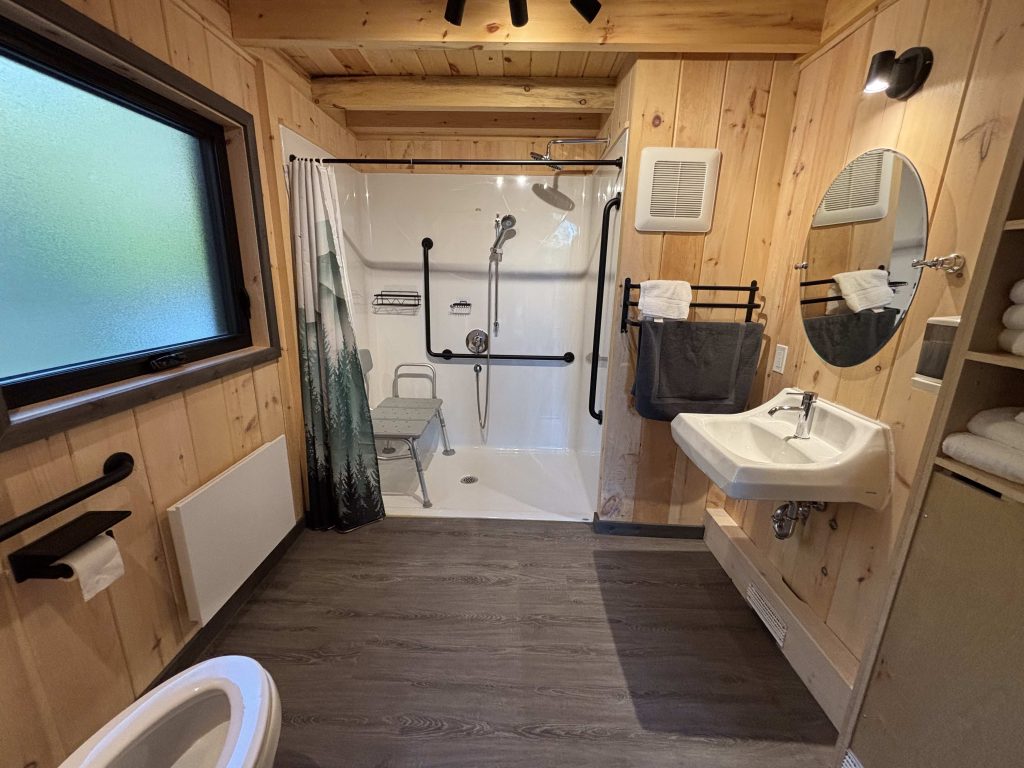 Salle de bain entièrement accessible avec douche sans seuil, barre d’appui, siège de douche et lavabo adapté dans un chalet des Chalets Lanaudière.