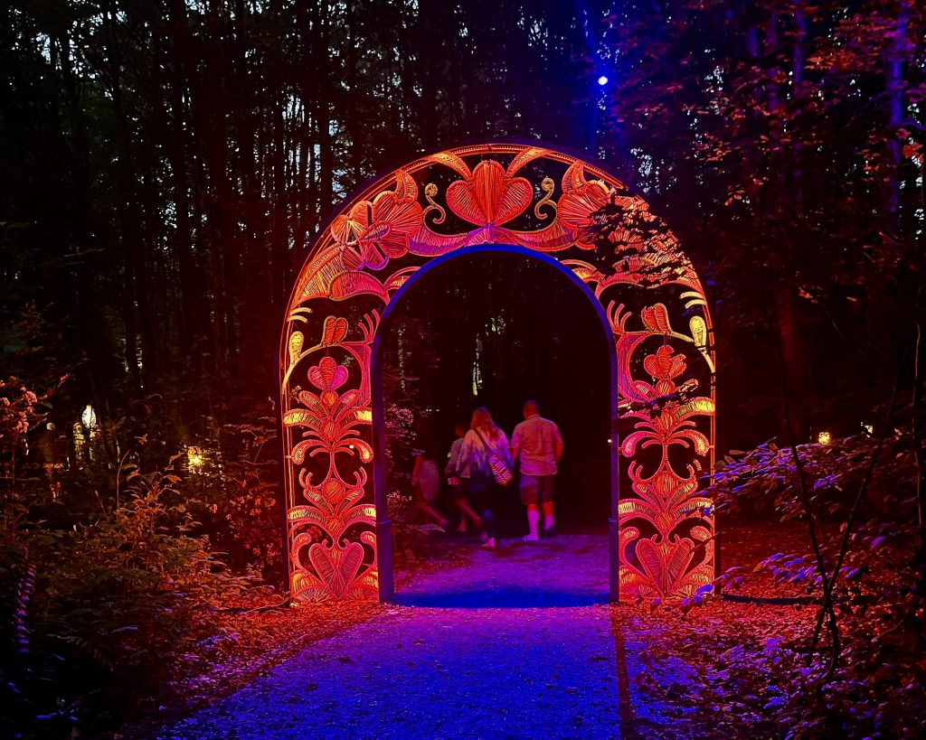 Portail décoratif rouge illuminé, situé dans une forêt sombre, permettant une promenade immersive et accessible en hiver.